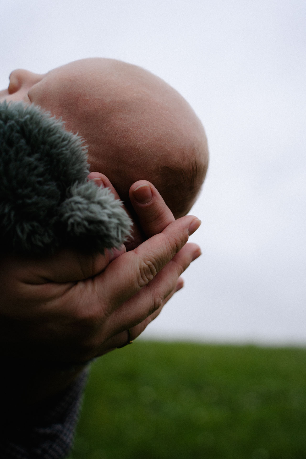 Der Kopf eines Neugeborenen, der in den Händen seiner Mutter liegt, in der Natur aufgenommen, im Rahmen der Newborn- und Familienfotografie.