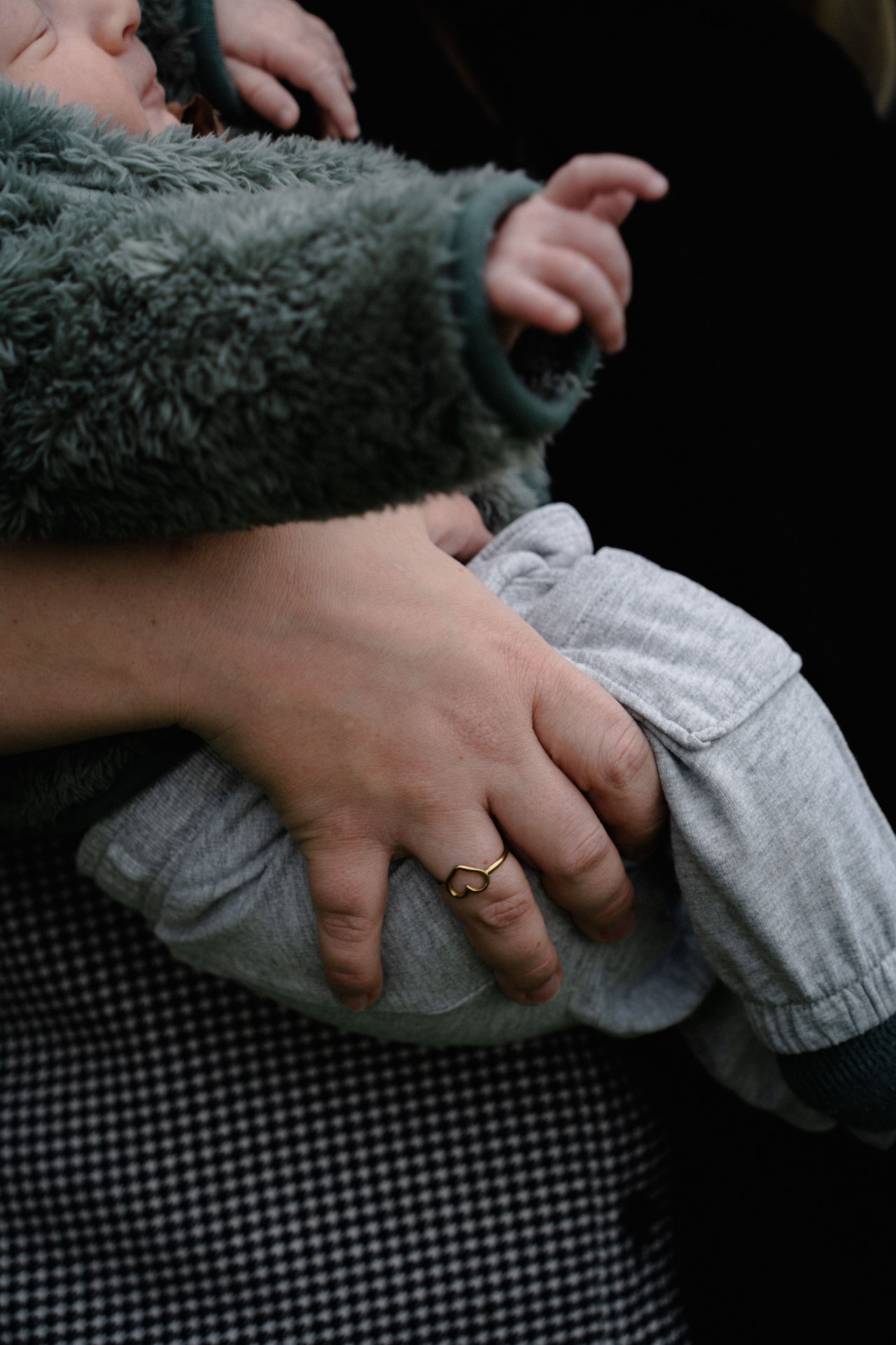 Die Hand einer Mutter, die ihren Sohn auf den Armen trägt, am Finger trägt sie einen Herz-Ring. Das Foto ist im Rahmen der Newborn- und Familienfotografie entstanden.