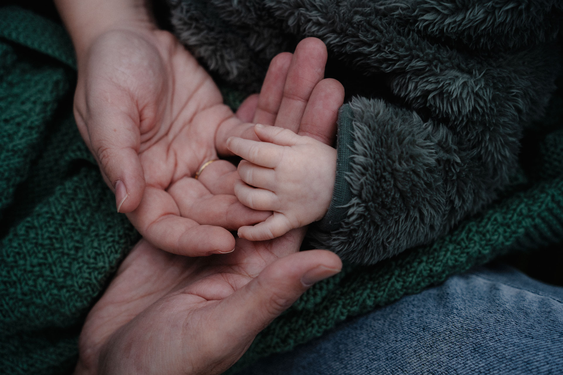 Die Hände von Vater, Mutter und einem Baby liegen ineinander, das Foto ist im Rahmen der Newborn- und Familienfotografie entstanden.