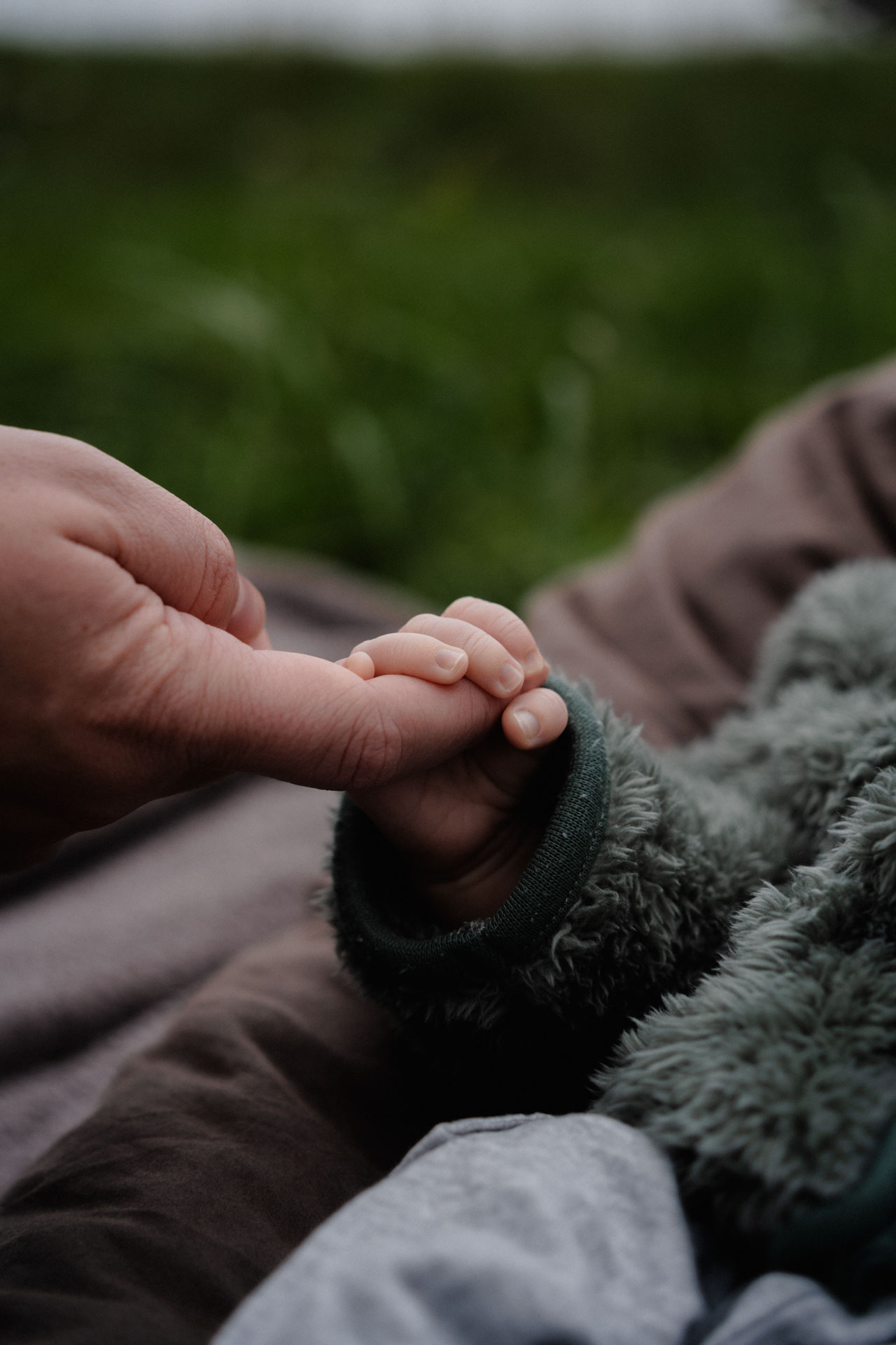 Ein Neugeborenes hält mit der ganzen Hand den Zeigefinger seiner Mutter umklammert, das Foto ist im Rahmen der Newborn- und Familienfotografie entstanden.