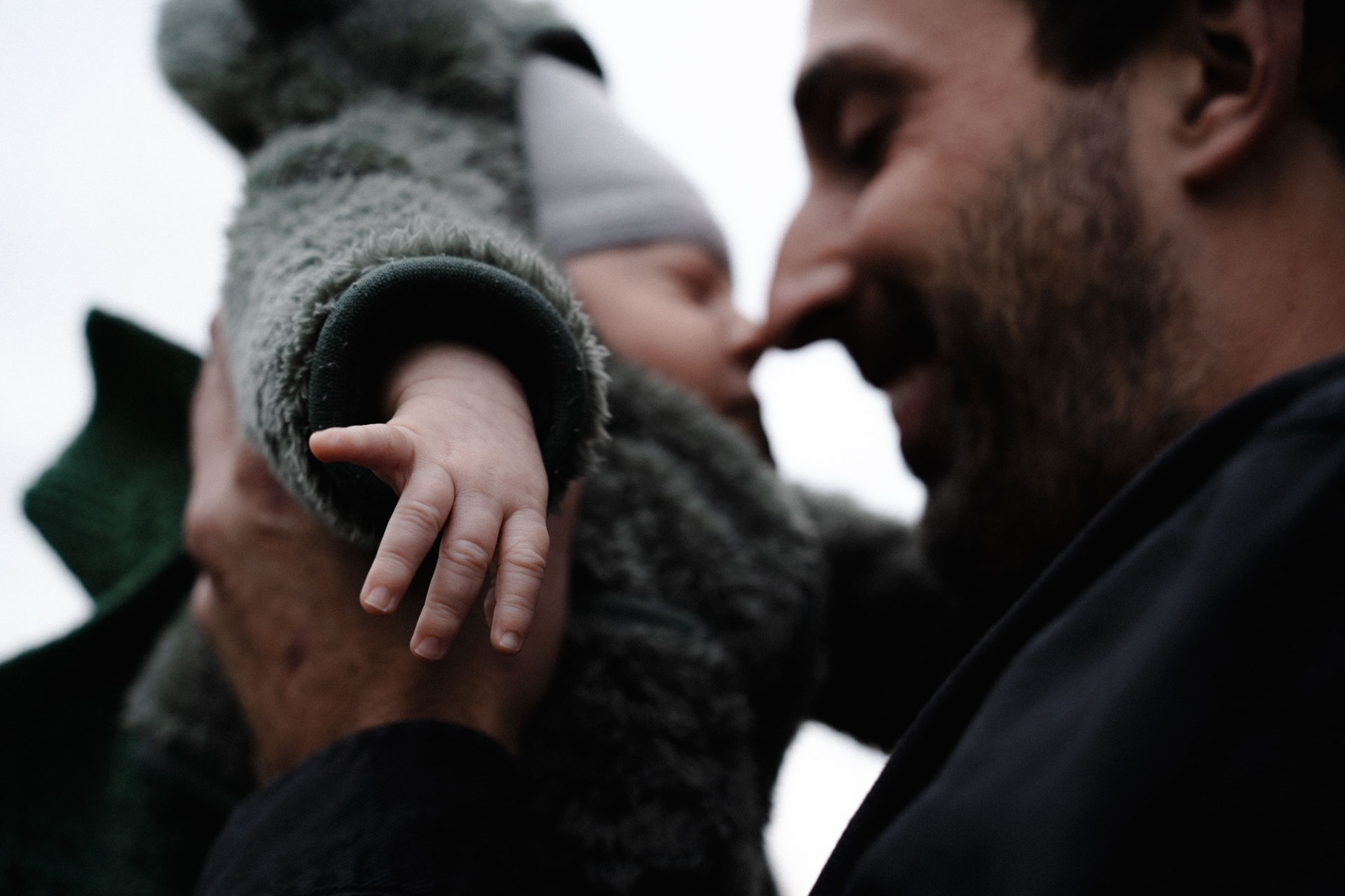 Vater und Sohn berühren sich an den Nasenspitze, der Fokus liegt auf der Hand des Neugeborenen, das Foto ist im Rahmen der Newborn- und Familienfotografie entstanden.