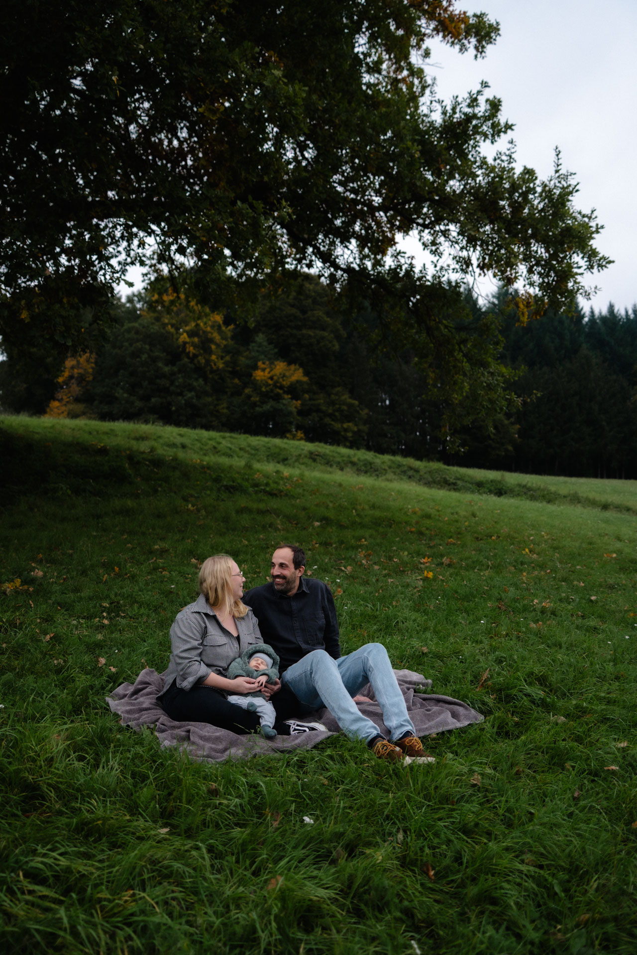 Eine junge Familie picknickt in einer schönen, herbstlichen Wiese, das Foto ist im Rahmen der Newborn- und Familienfotografie entstanden.