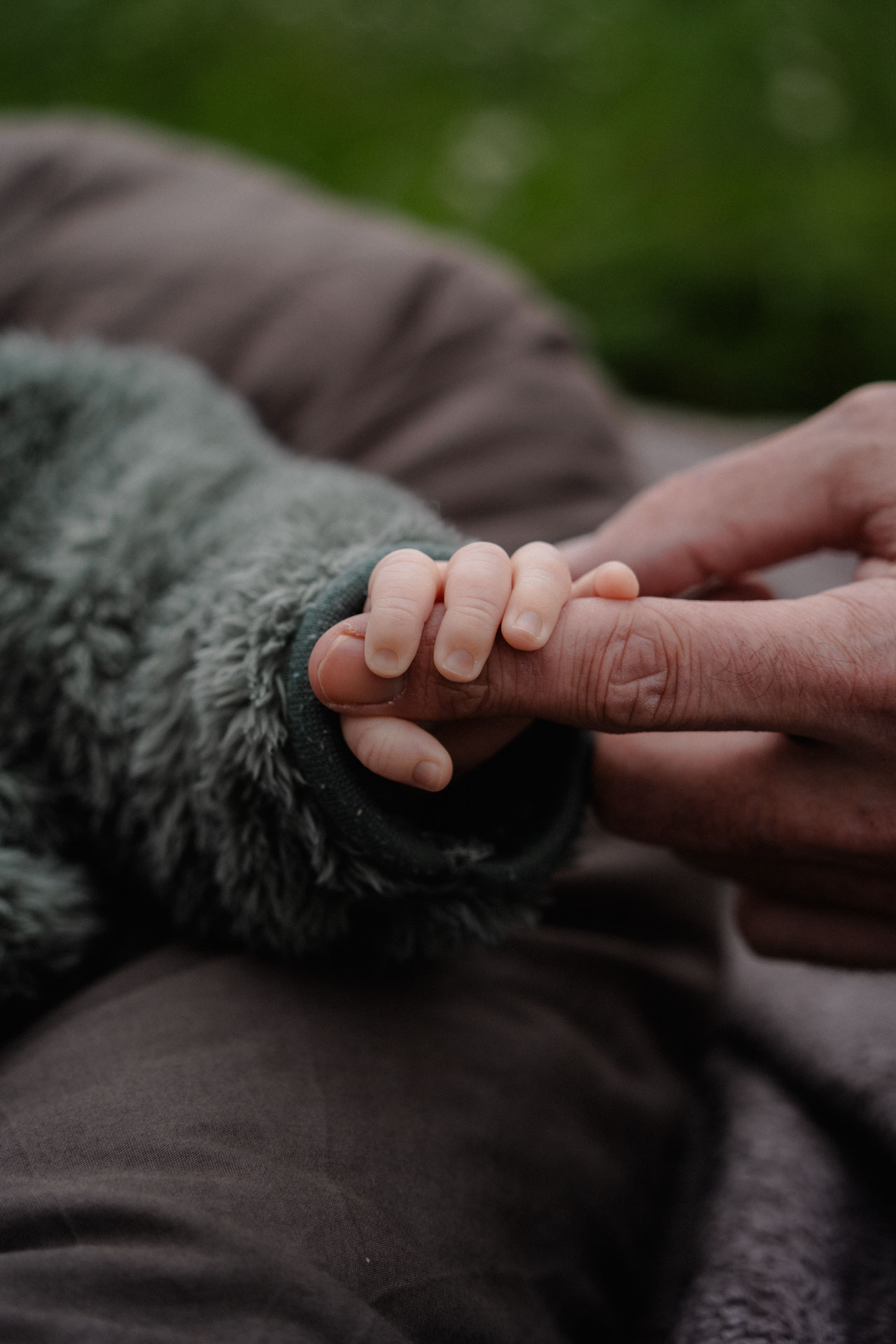 Die Hand eines Neugeborenen hält den Finger seines Vaters umklammert.