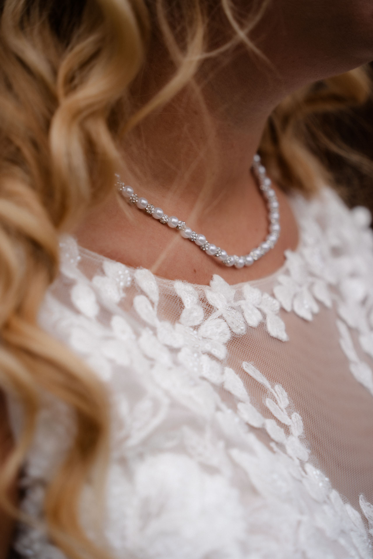 Eine Nahaufnahme der Kette der Braut, man sieht dezent die Spitze ihres Kleides und ihre Locken.