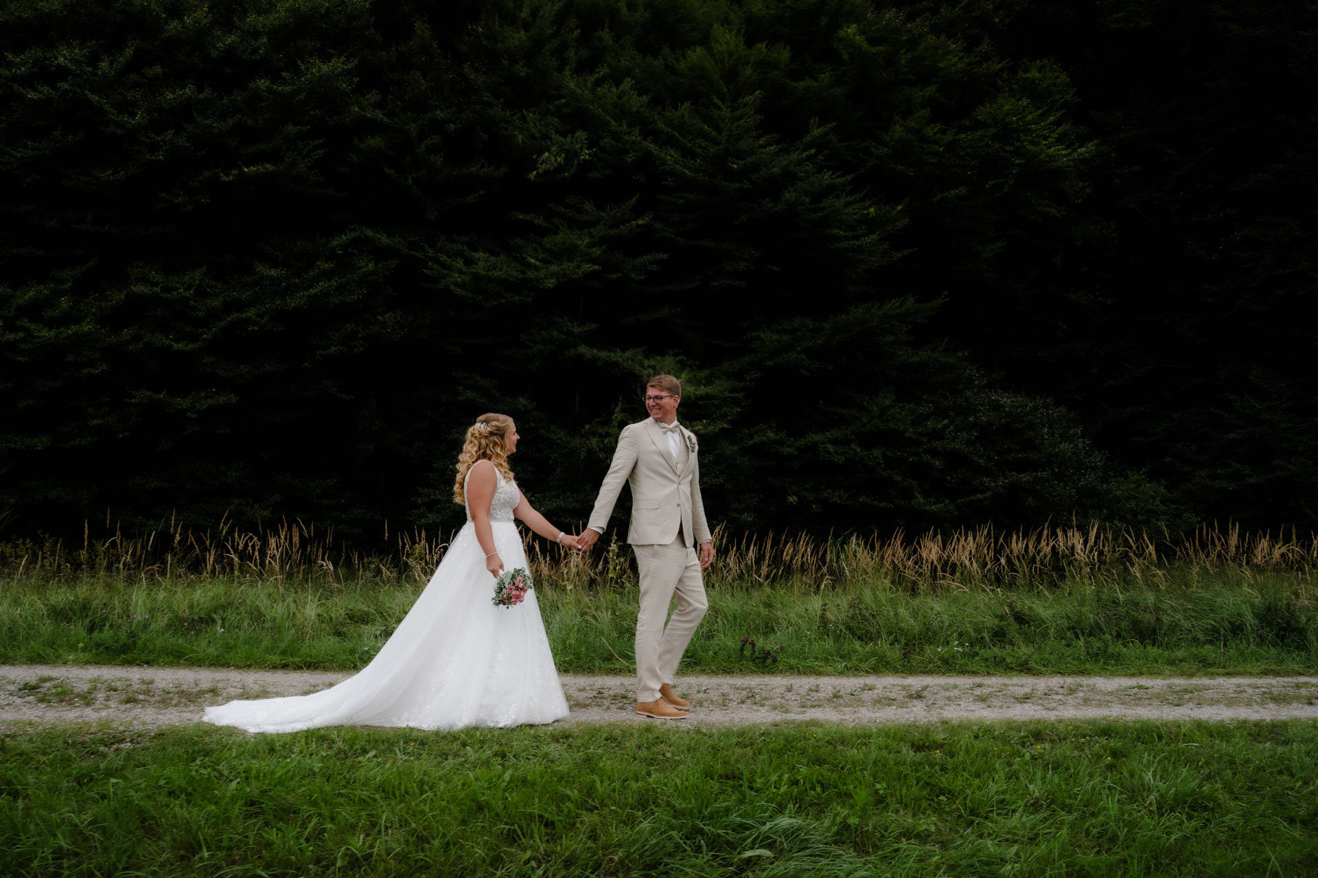 Der Bräutigam führt seine Braut einen Feldweg entlang.