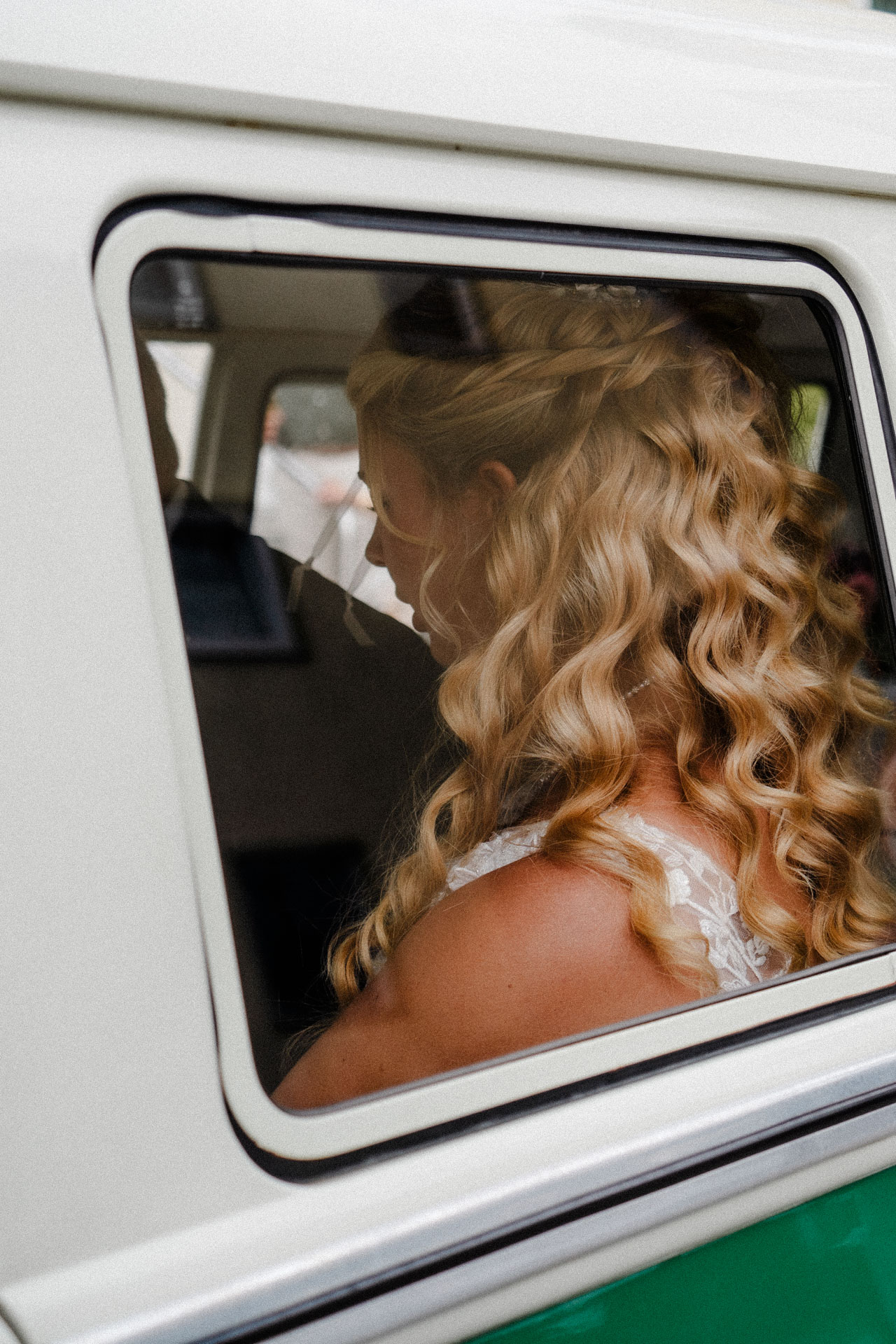 Eine Braut sitzt auf dem Rücksitz eines VW Oldtimers, die Hochzeitsfotografin hat das Foto durch das Fenster geschossen.