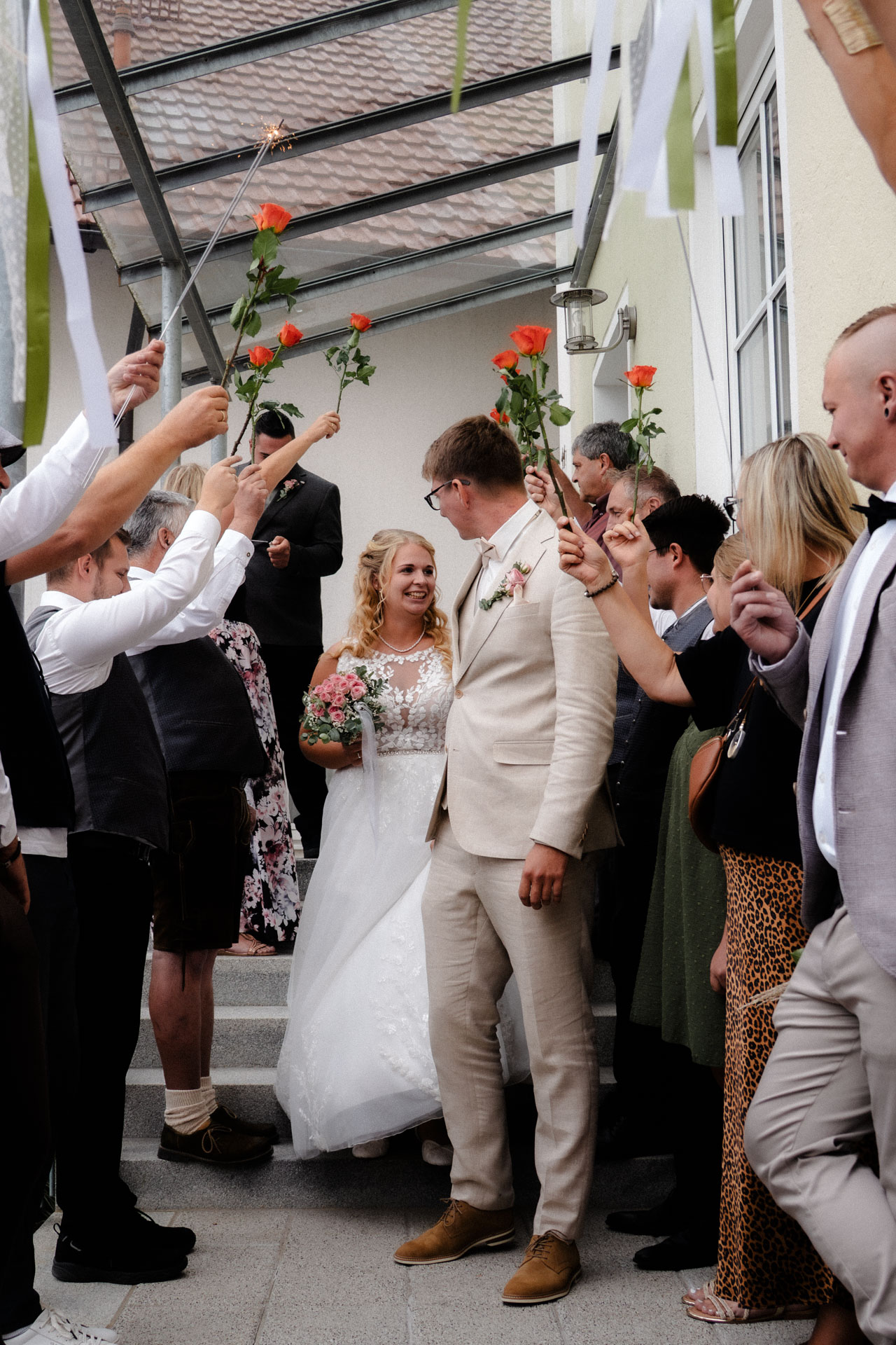Das frisch vermählte Paar verlässt nach der Hochzeit das Standesamt und wird von Freunden und Familien überrascht, die Rosen in die Lüfte halten.