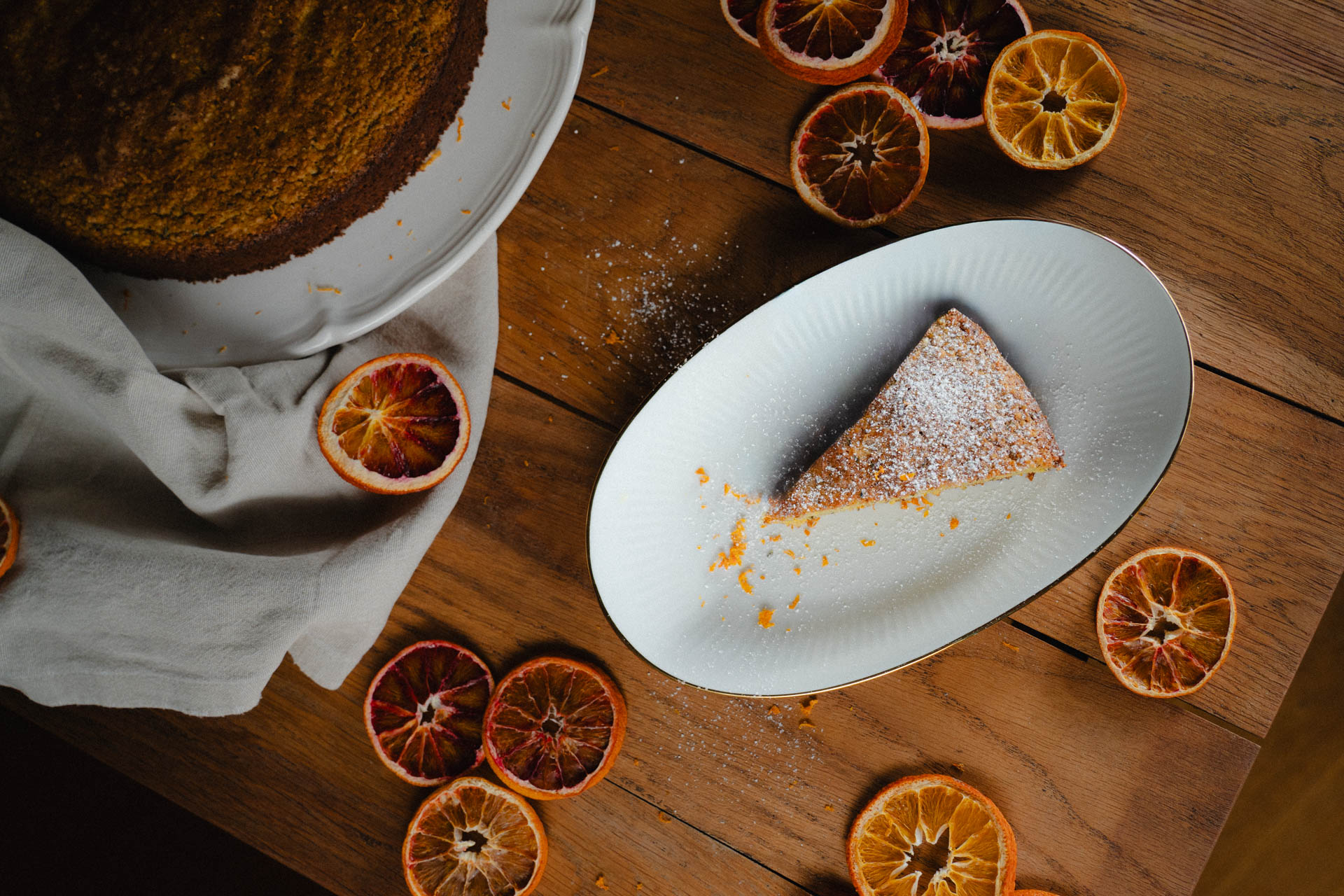 Das Foto eines Orangenkuchens, stilvoll arrangiert auf einem Tisch mit getrockneten Orangenscheiben, das Foto ist im Rahmen der Produkt-, Werbe und Foodphotography entstanden.