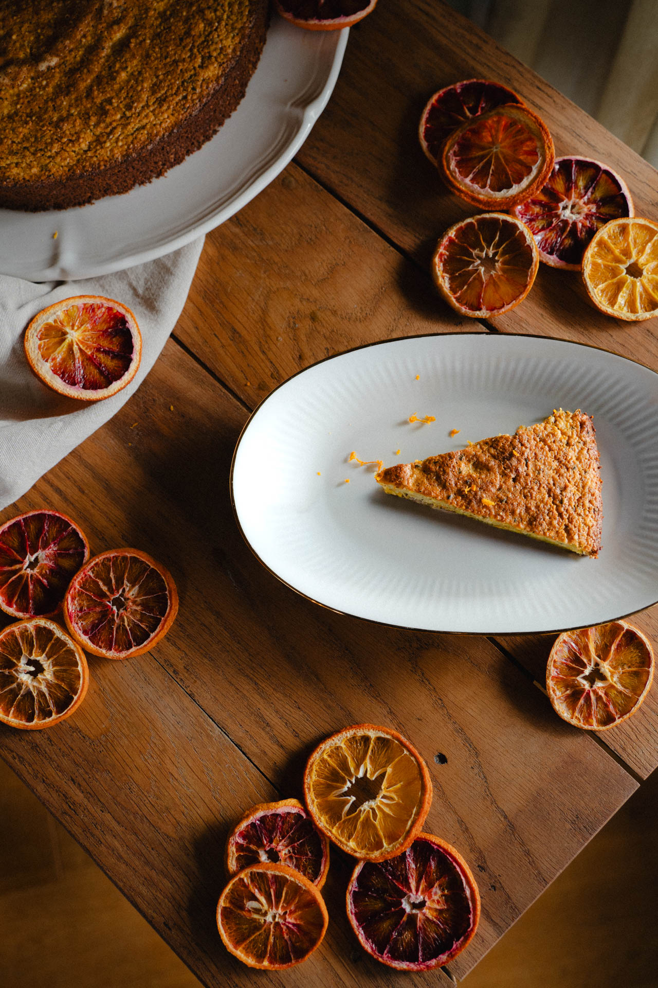Das Foto eines Orangenkuchens, stilvoll arrangiert auf einem Tisch mit getrockneten Orangenscheiben, das Foto ist im Rahmen der Produkt-, Werbe und Foodphotography entstanden.
