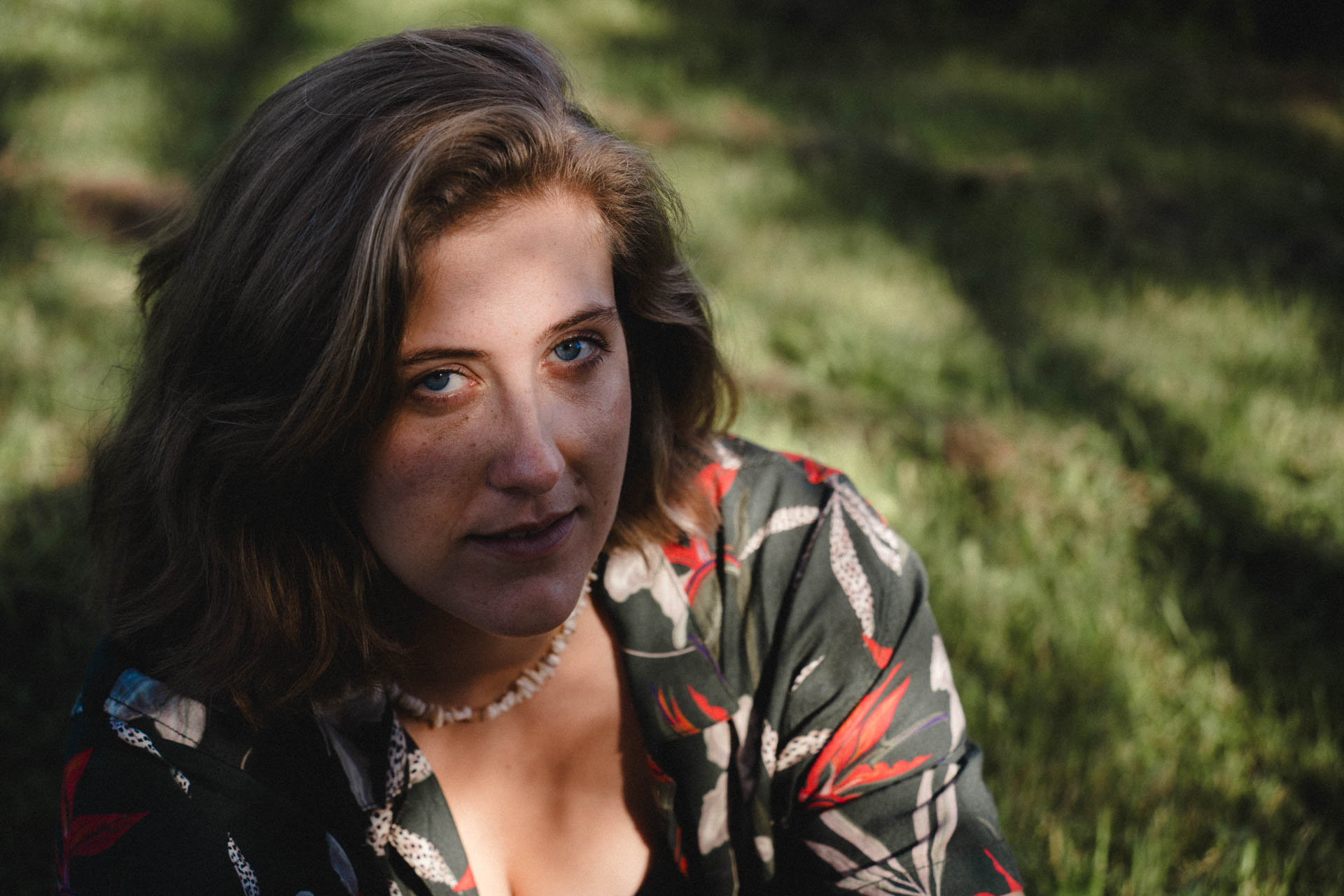 Eine Frau die auf einer Wiese sitzt, die Sonne beleuchtet ihre Augen. Das Foto ist im Rahmen der Portraitfotografie entstanden.