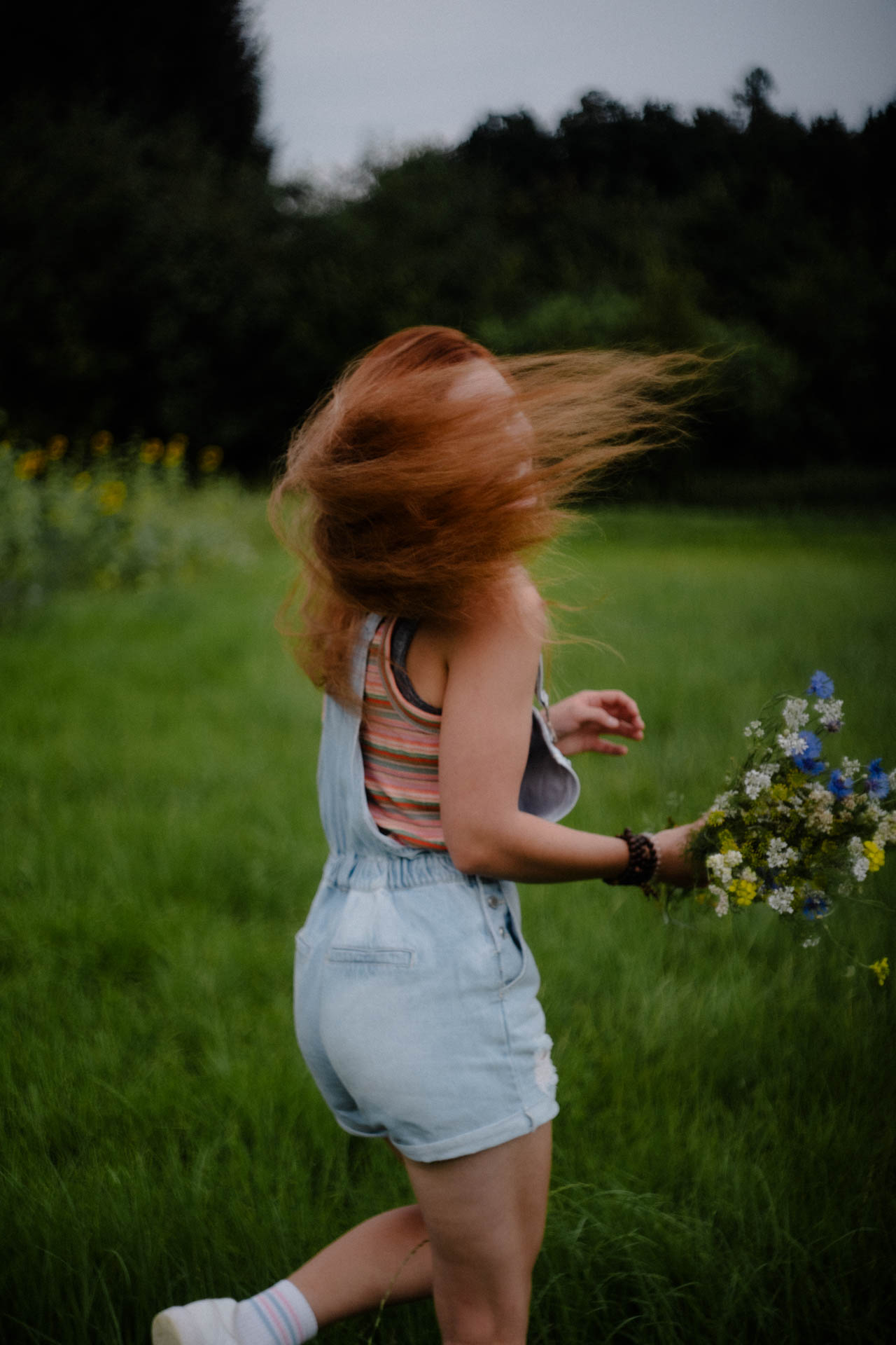 Das verschwommene Foto einer Frau, die über eine Blumenwiese rennt. Das Foto ist im Rahmen der Portraitfotografie entstanden.