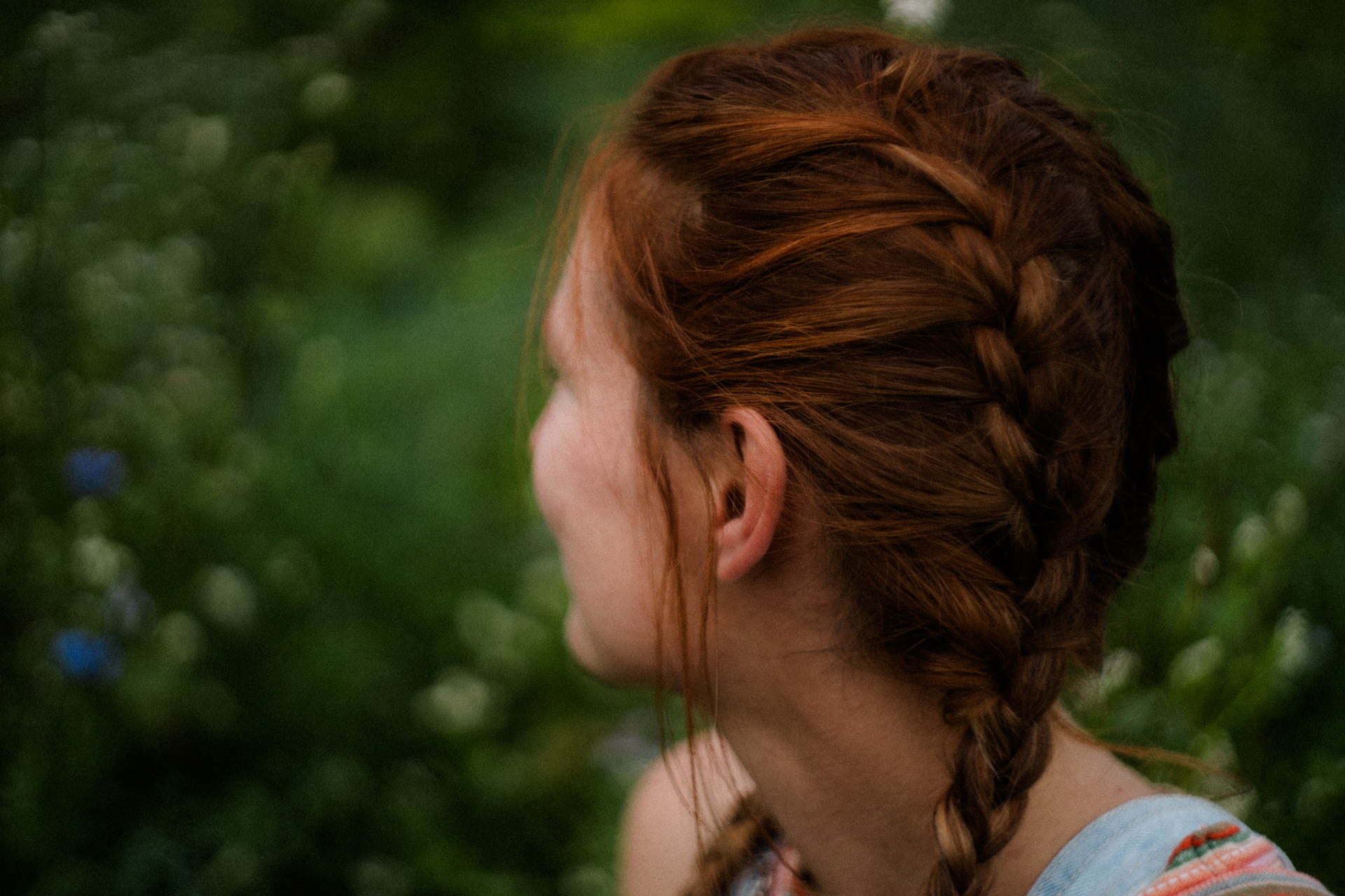 Das stimmige Foto einer Frau mit Zöpfen, die in einer Blumenwiese sitzt, das Foto ist im Rahmen der analogen Portraitfotografie entstanden.