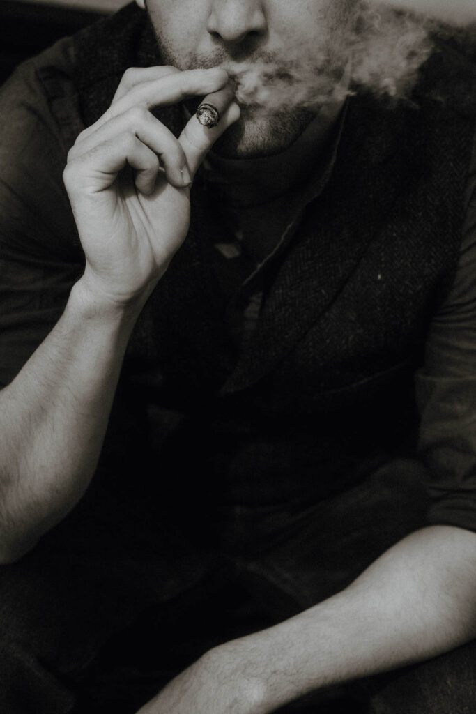 Das Portrait eines Mannes, der eine Zigarre raucht. Das Foto ist altmodisch und nostalgisch und wirkt analog.