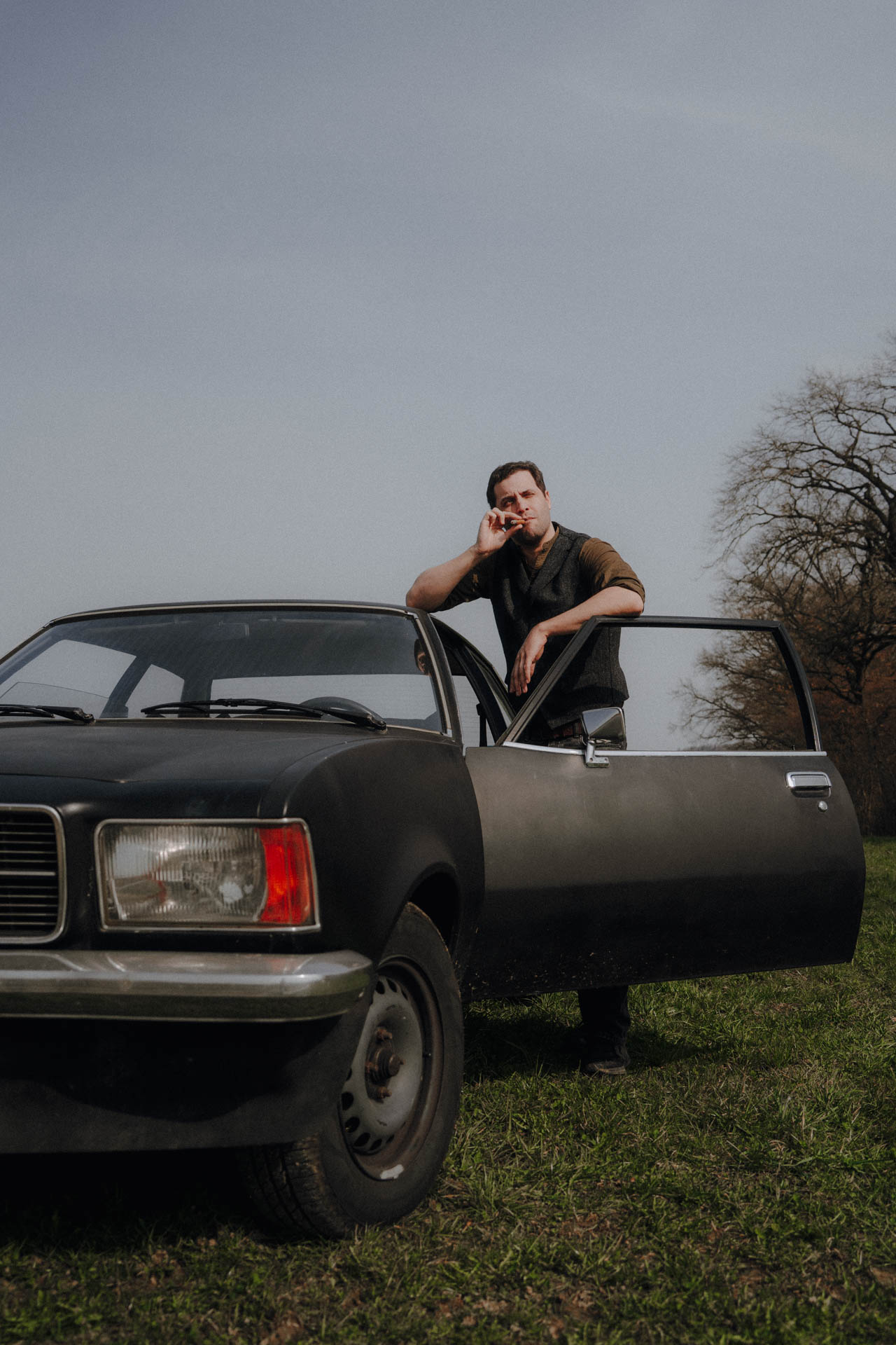 Ein Mann steht bei einem Oldtimer Opel Rekord und raucht eine Zigarre. Das Foto ist im Rahmen der Portraitfotografie entstanden.