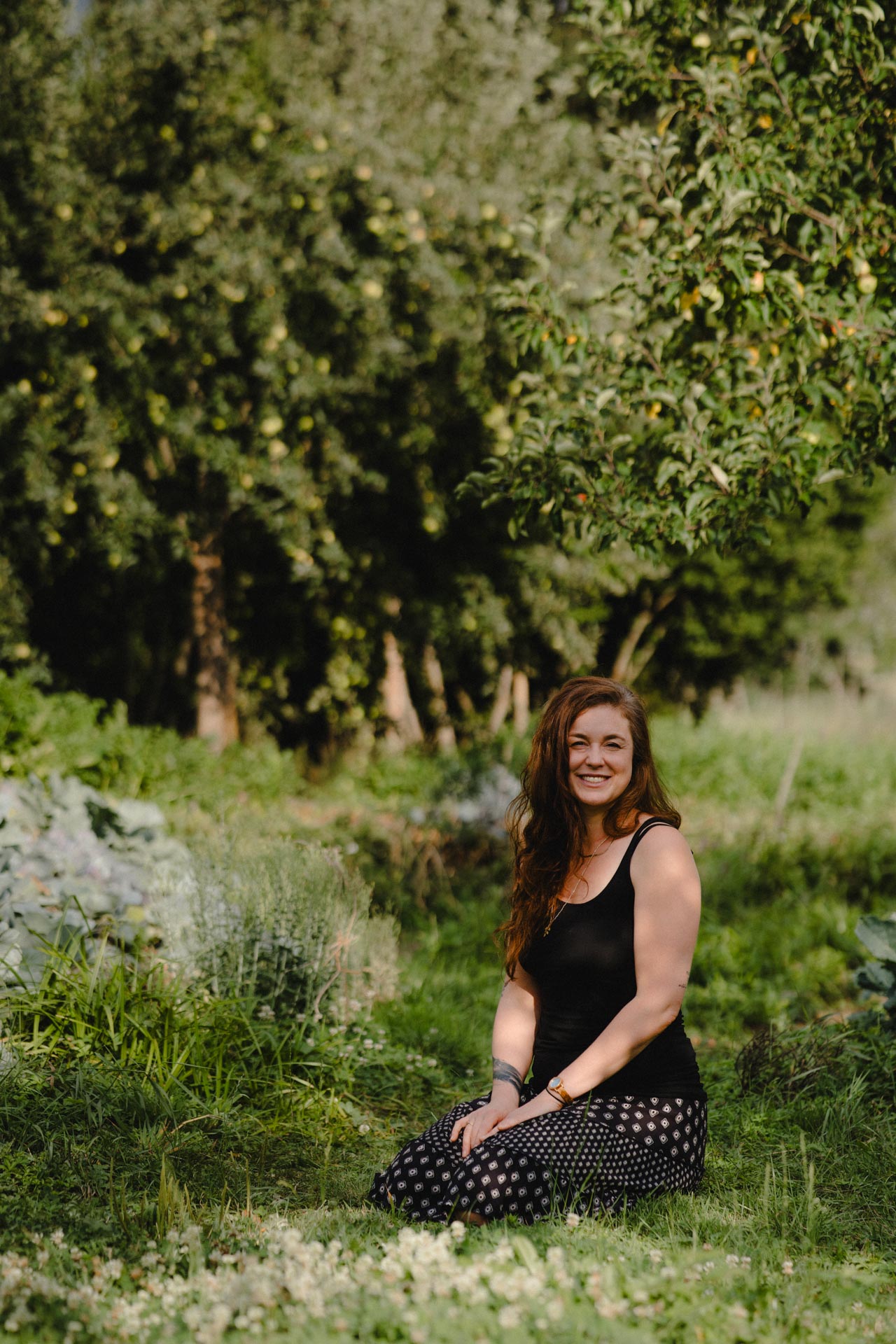 Eine Frau sitzt auf einer Wiese in der Sonne, es ist Sommer, alles blüht, das Foto ist im Rahmen der Portrait- und Businessfotografie entstanden.